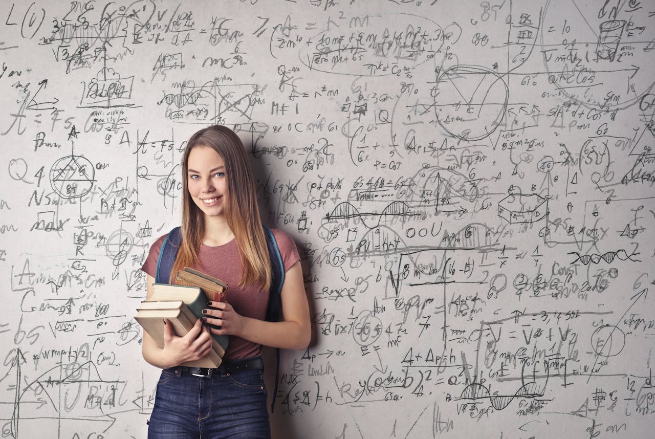 portfolio-03 Young woman holding books standing in front of a chalkboard filled with mathematical formulas.